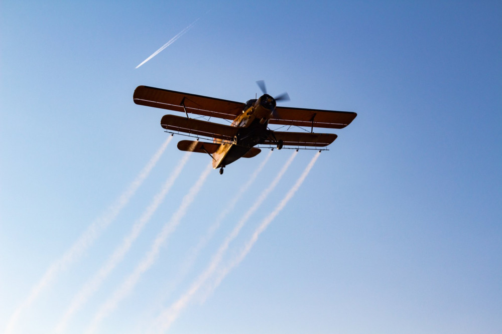 Antonov An-2 single-engine biplane spraying mosquitocide chemical over the city