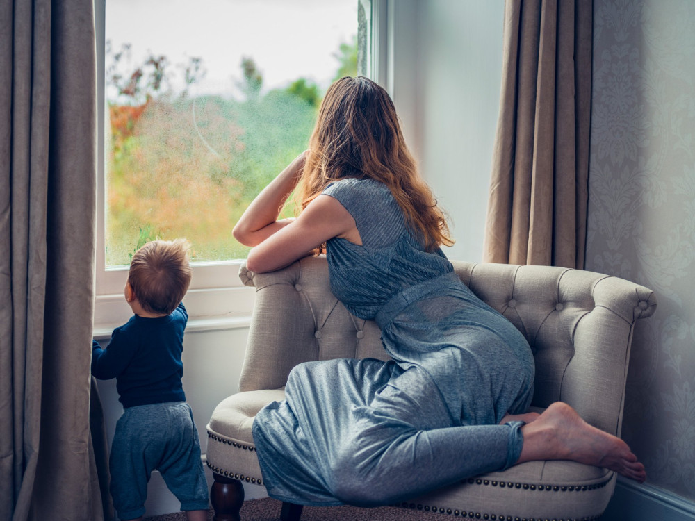 A young mother wearing an elegant dress is by the window with her baby