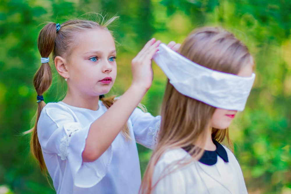 Funny girls play blind man's buff outdoors in the forest.