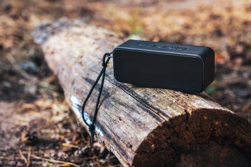 Portable wireless bluetooth speaker for listening to music on a log in the forest
