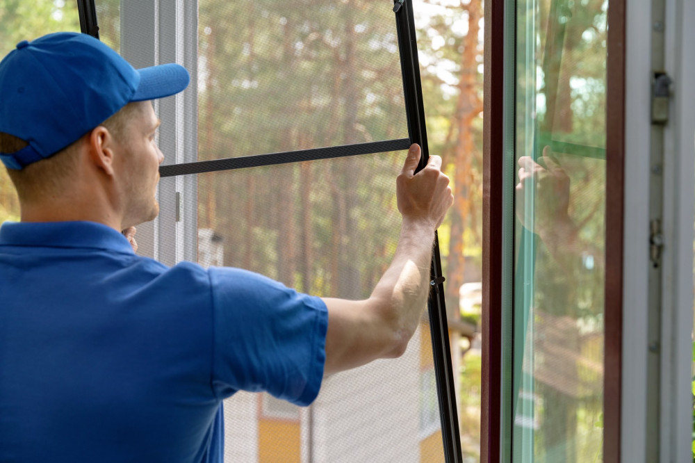 worker installing mosquito net wire mesh in plastic window frame